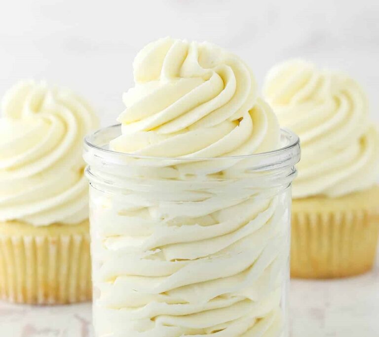 A jar filled with creamy vanilla frosting and cupcakes in the background.