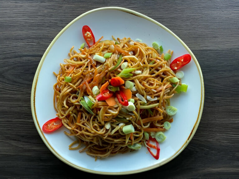 Plate of delicious stir-fried noodles garnished with vegetables and chili.