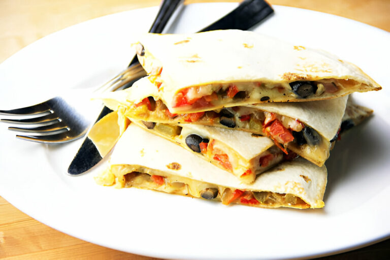 A plate of cut quesadillas with black beans, vegetables, and melted cheese, served with a fork and knife.