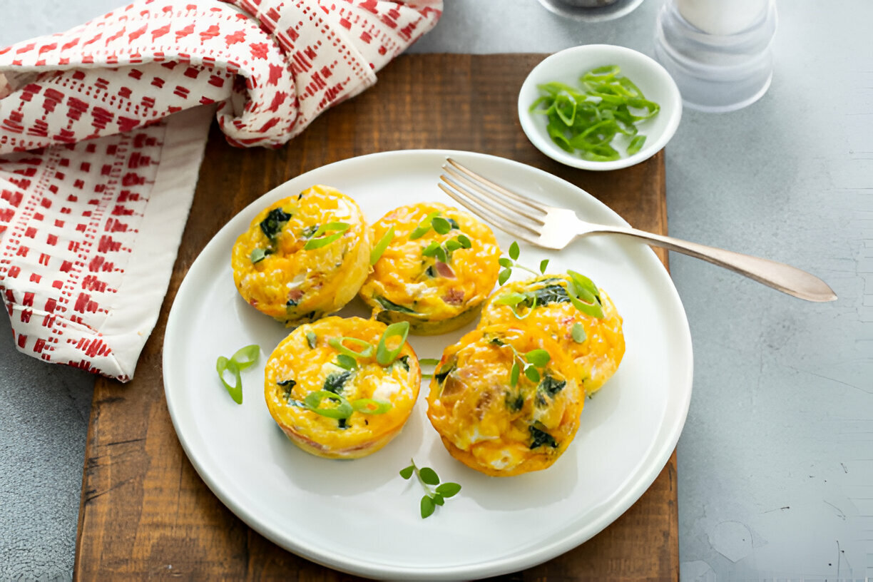 A plate of mini frittatas topped with green onions, served with a fork and a side of chopped green onions.