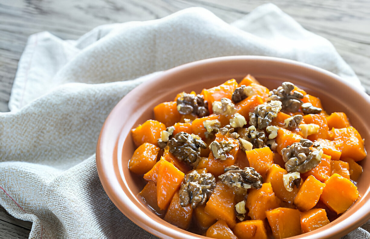 A bowl of diced butternut squash topped with walnuts, placed on a textured cloth.