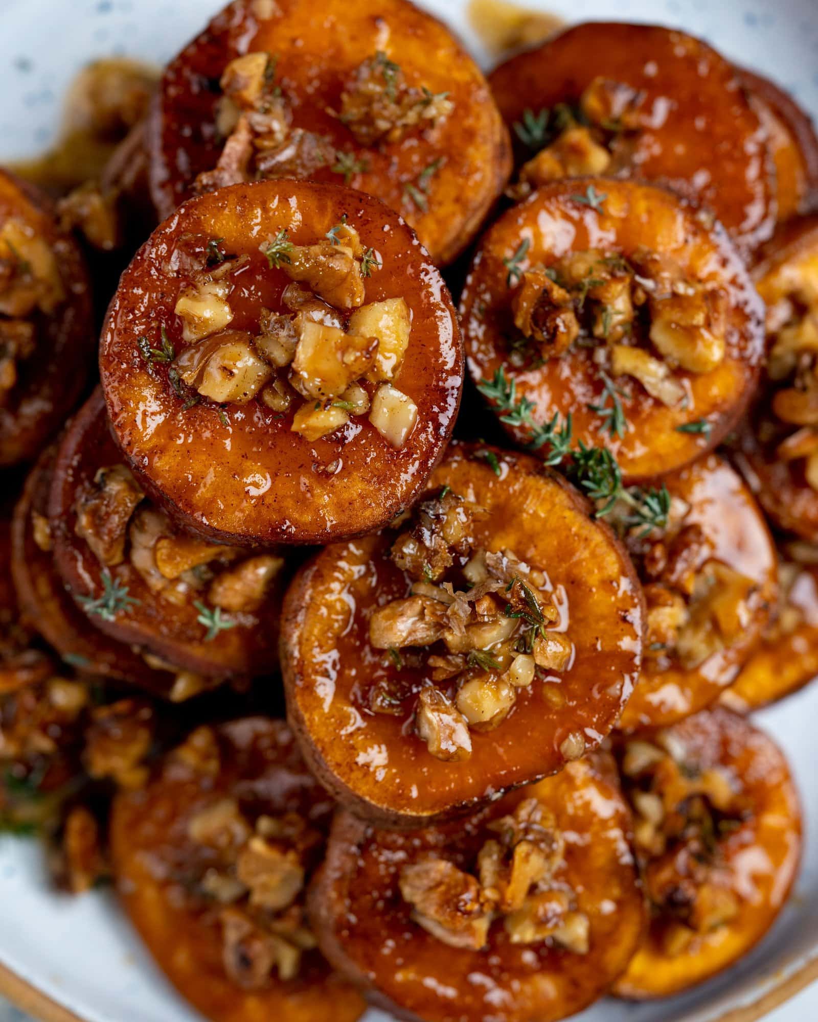 A close-up of sliced sweet potatoes topped with chopped nuts and a glossy syrup.