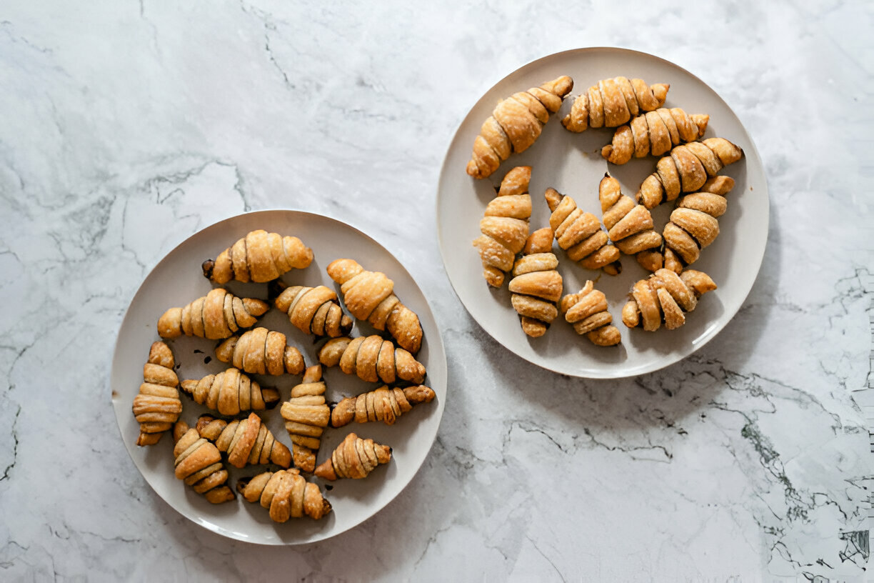 Two plates of freshly baked croissants on a marble countertop.