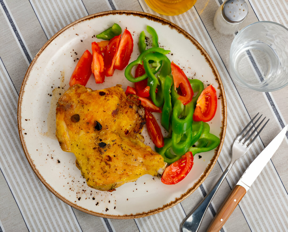 A delicious plate of fried chicken served with fresh green and red bell peppers and sliced tomatoes.